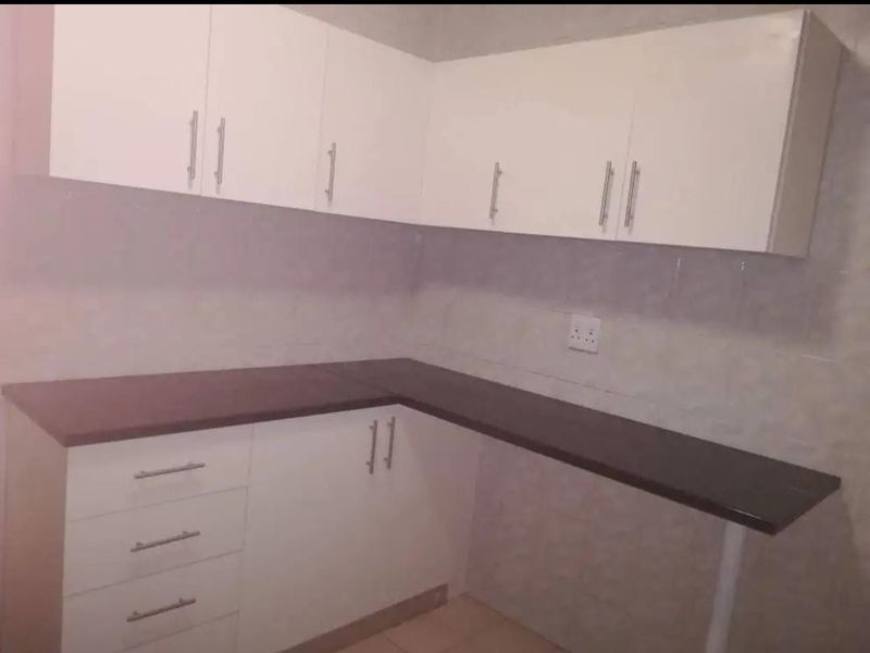 A clean, empty kitchen featuring white built-in cabinetry, dark laminate countertops, and a tiled backsplash.