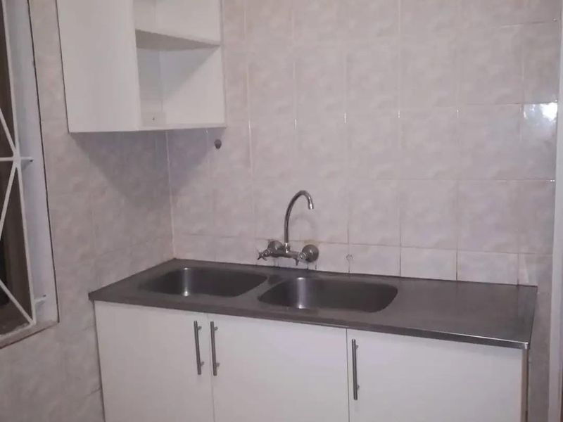 A compact kitchen area featuring a stainless steel double sink, built-in base and wall cabinetry, and tiled wall finishes.