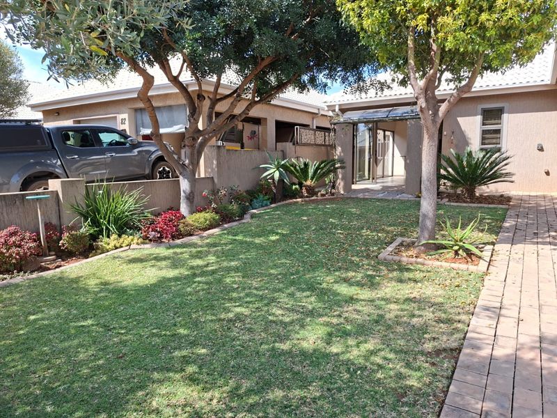 Front view of a townhouse featuring a well-maintained garden, paved driveway, and a covered entrance area with established trees.