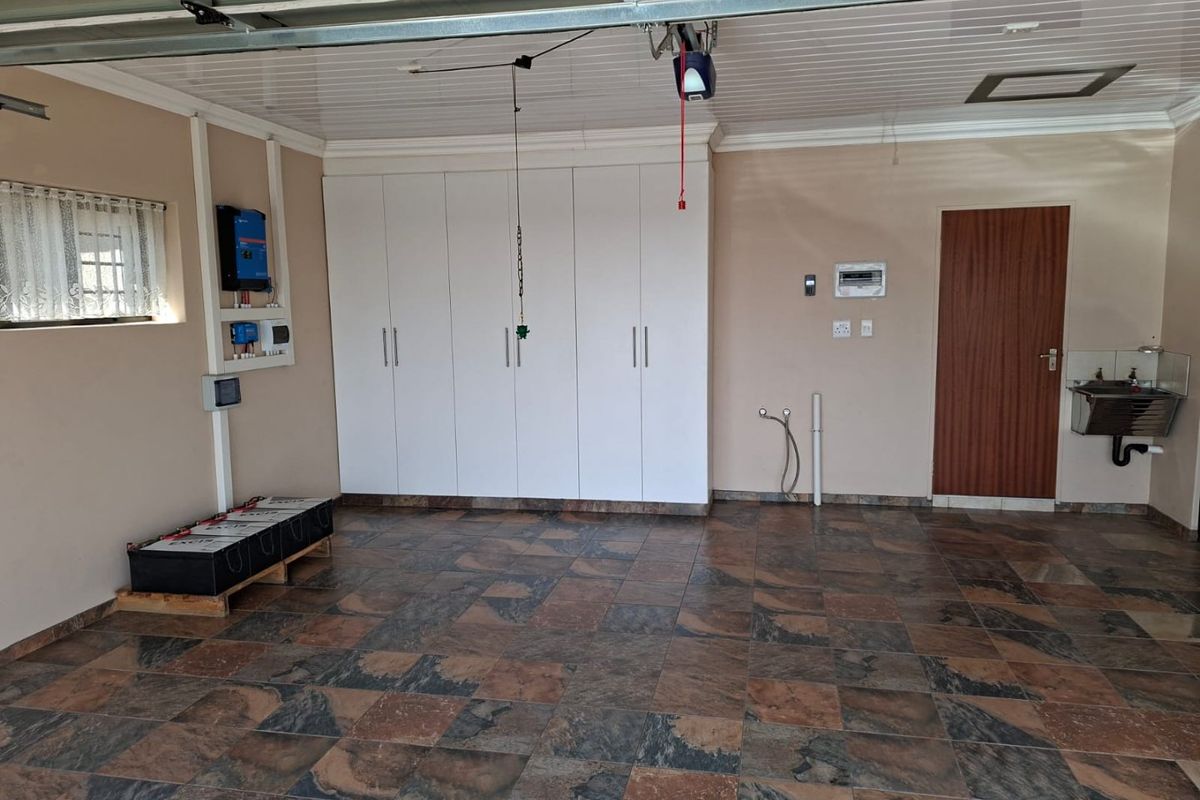 Spacious garage featuring tiled flooring, extensive built-in storage cabinetry, a wall-mounted utility sink, and an integrated solar power system with battery storage.