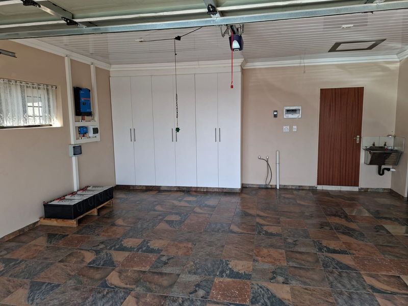 Spacious garage featuring tiled flooring, extensive built-in storage cabinetry, a wall-mounted utility sink, and an integrated solar power system with battery storage.