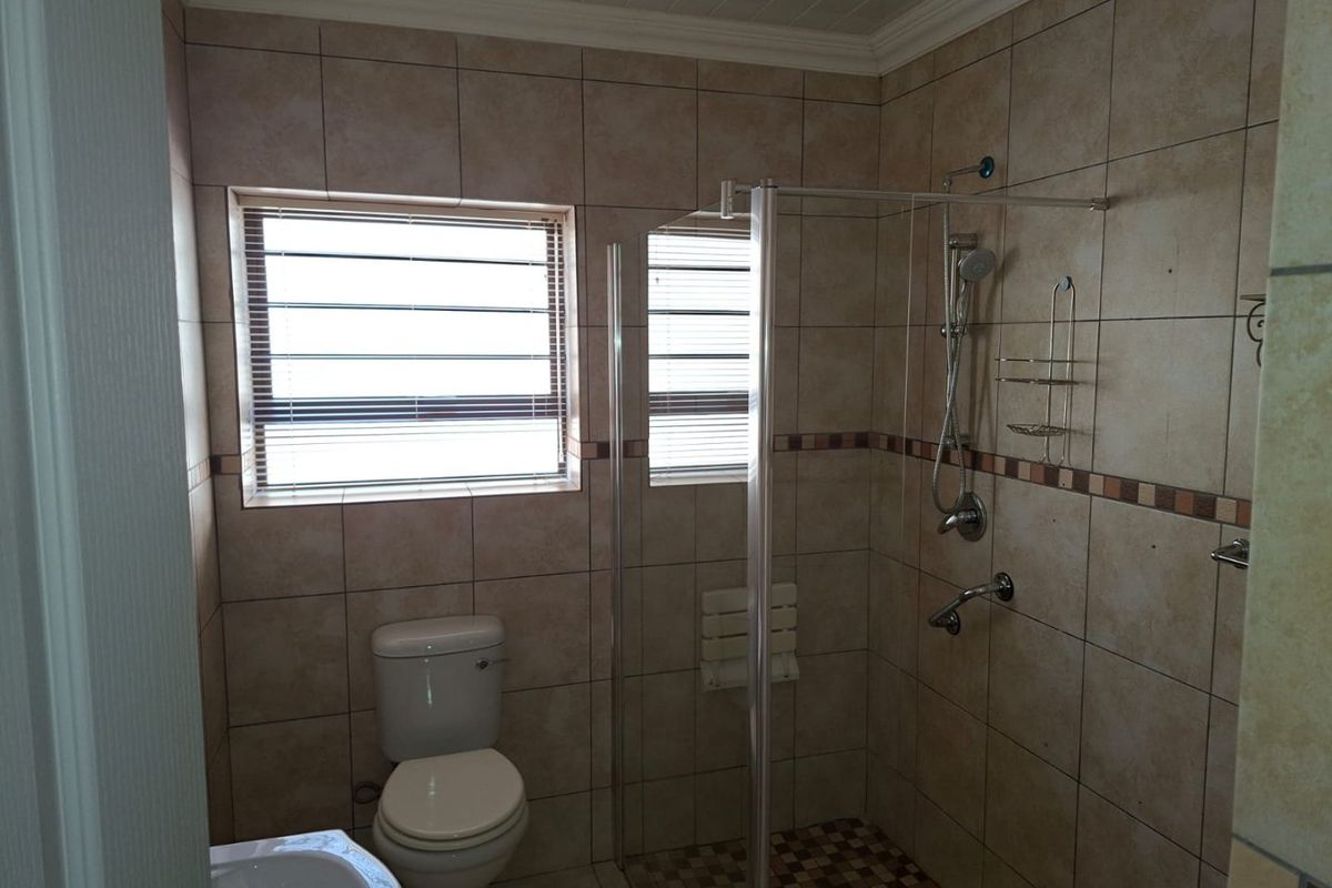 A functional bathroom featuring a walk-in shower with glass screen, tiled walls and flooring, and a standard toilet.