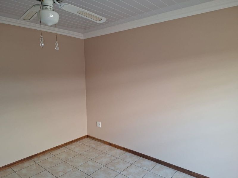 An empty bedroom featuring tiled flooring, a ceiling fan, and neutral wall tones, providing a blank canvas for personalization.