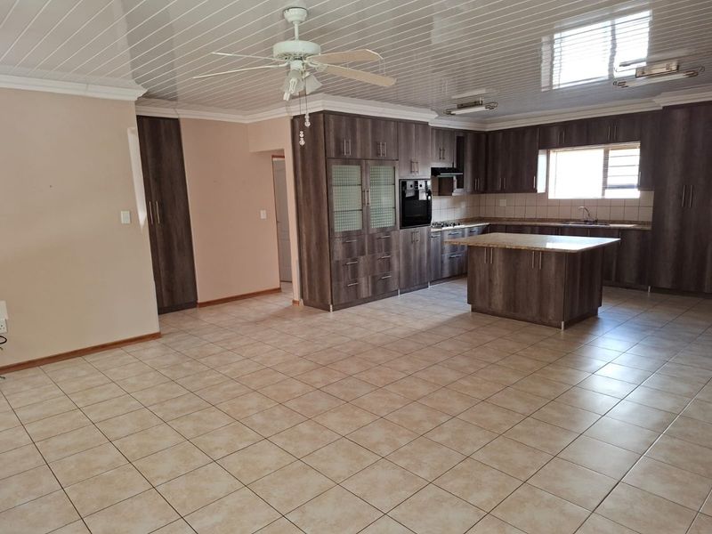 Spacious open-plan kitchen and living area featuring dark wood cabinetry, granite countertops, built-in appliances, and neutral tiled flooring throughout.