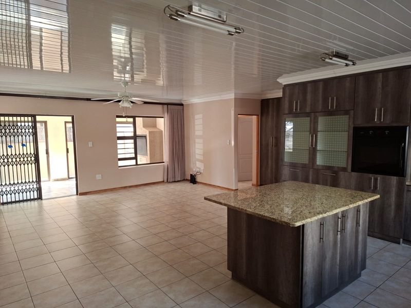 Spacious open-plan living area featuring a modern kitchen with granite island, built-in oven, tiled flooring, and direct access to an outdoor patio area.