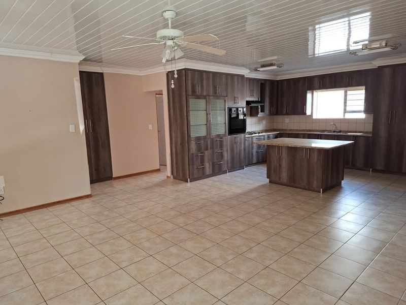 Spacious open-plan kitchen and living area featuring dark wood cabinetry, granite countertops, a central island, and tiled flooring throughout.