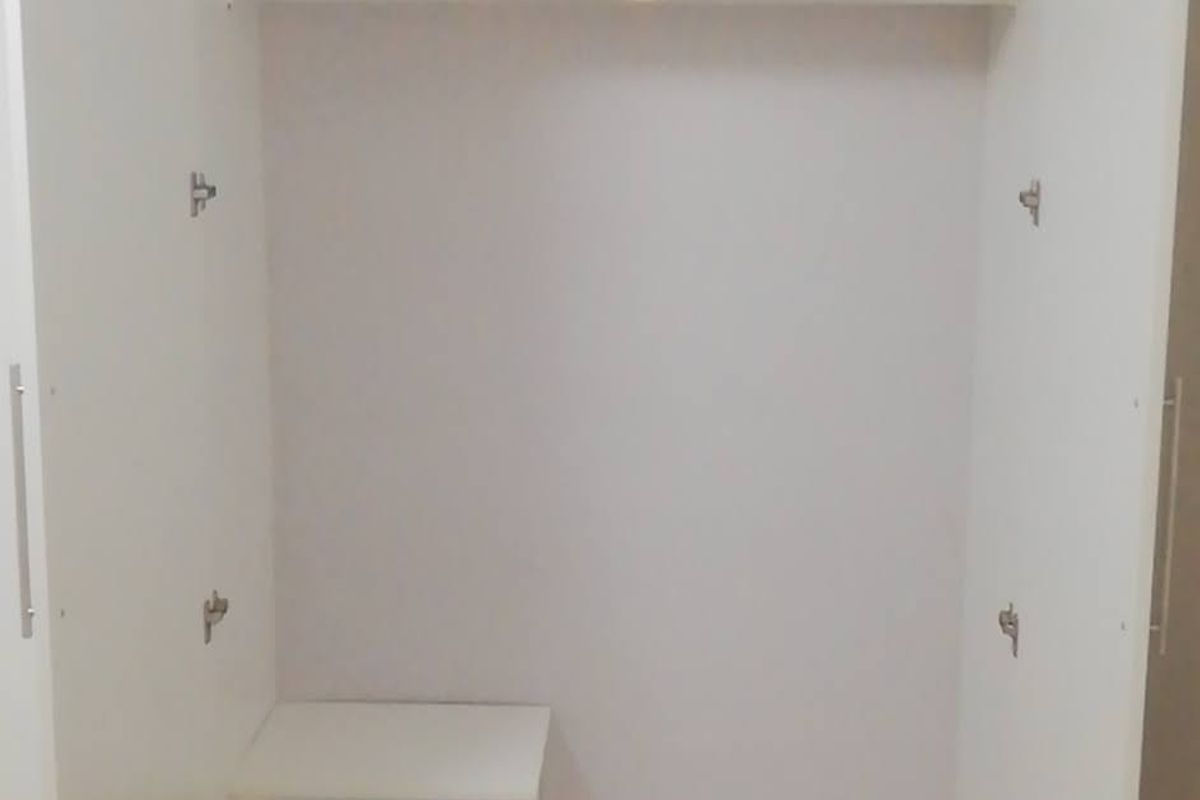 A clean, white built-in wardrobe featuring internal shelving and integrated drawers, providing efficient storage space within the bedroom.