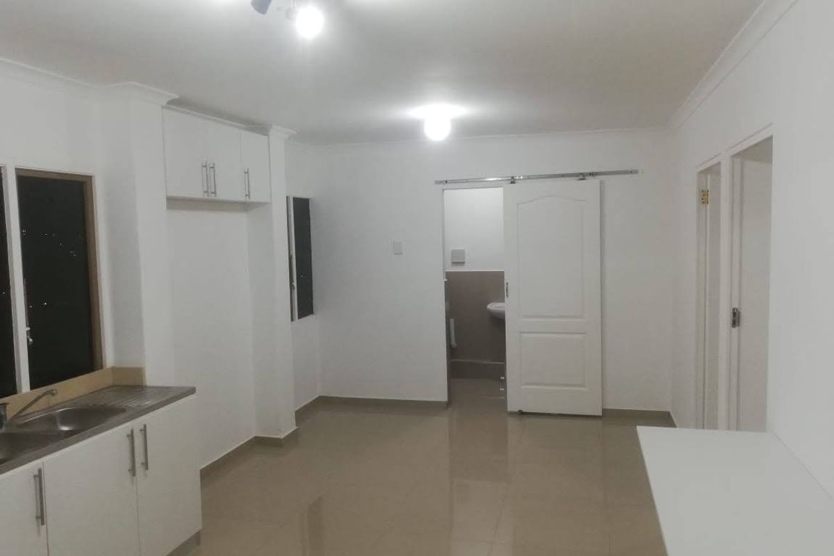 An open-plan living and kitchen area featuring tiled flooring, white cabinetry, and a sliding door leading to an adjacent room.