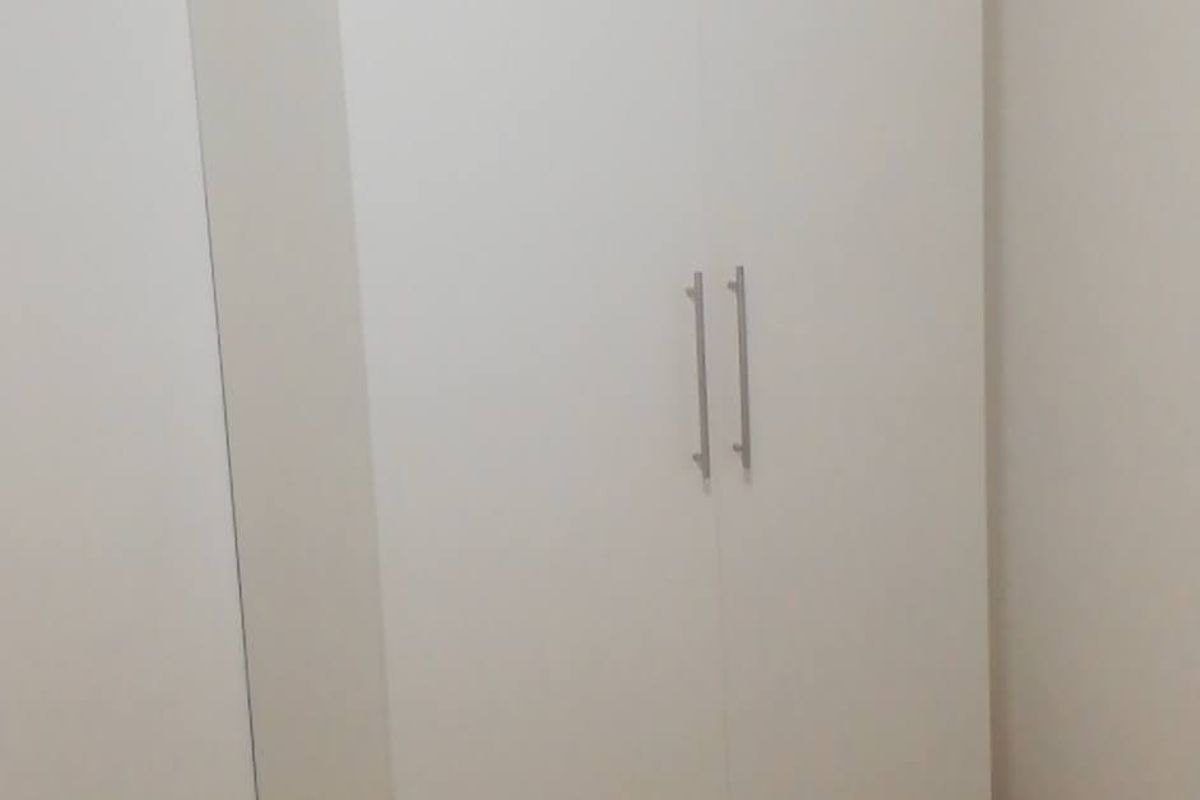 A clean, minimalist bedroom featuring a white built-in wardrobe and neutral tiled flooring.