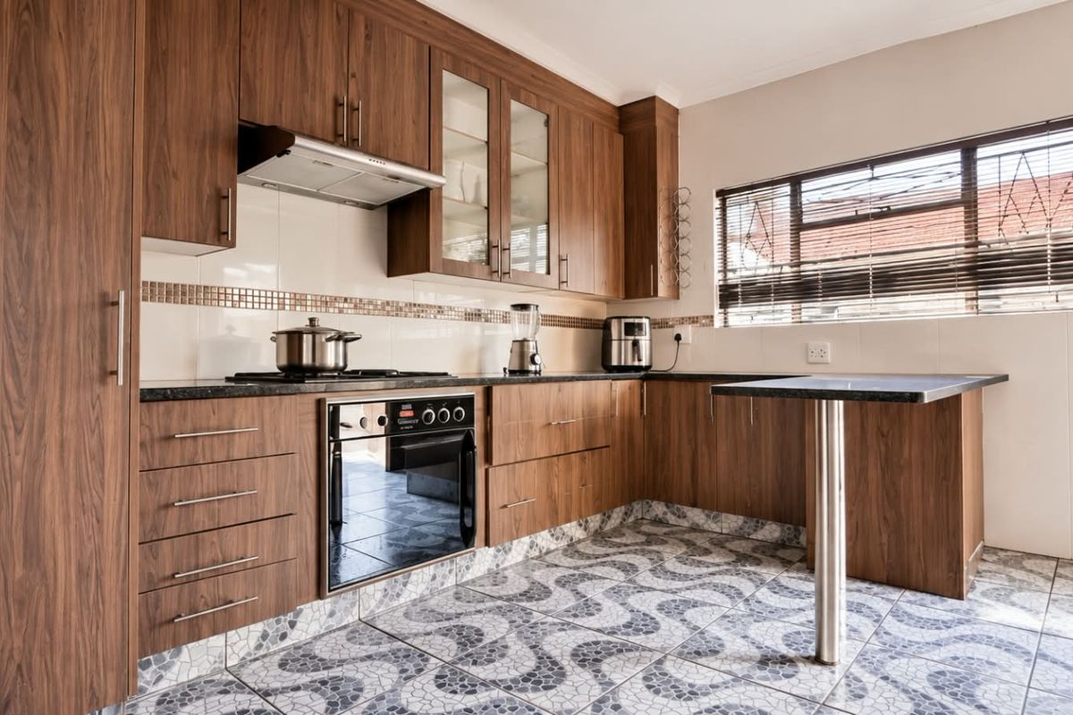 A functional kitchen featuring wood-finish cabinetry, dark countertops, a built-in oven with gas hob, and patterned tiled flooring with an integrated breakfast bar.