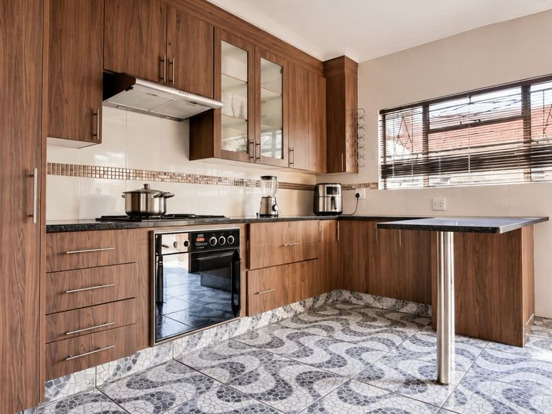 A functional kitchen featuring wood-finish cabinetry, dark countertops, a built-in oven with gas hob, and patterned tiled flooring with an integrated breakfast bar.