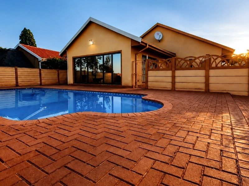 A well-maintained outdoor pool area featuring brick paving, a private boundary wall, and direct access to the home via large sliding glass doors.