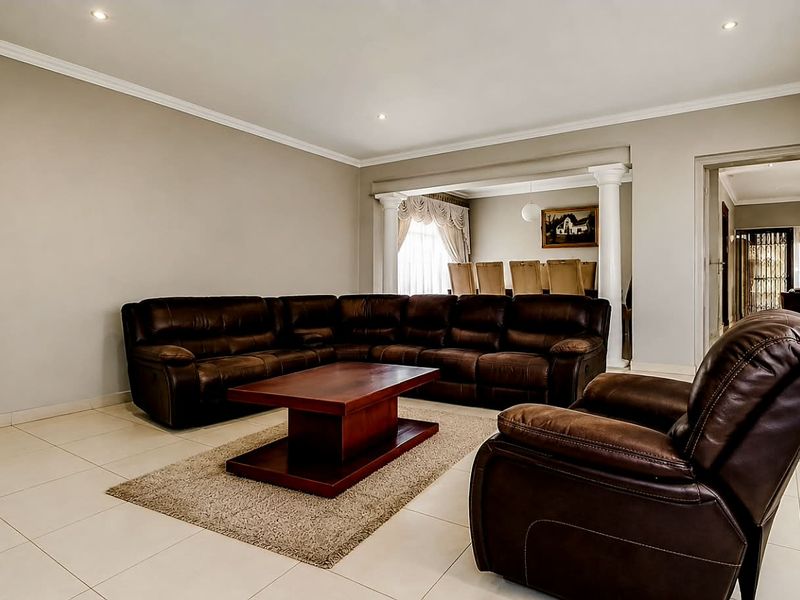 Spacious living room featuring neutral tiled flooring, recessed downlighting, and decorative columns leading into an adjacent dining area.