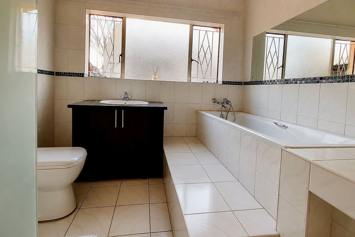 A functional bathroom featuring a built-in vanity, drop-in sink, and a tiled bathtub surround with a large wall-mounted mirror.