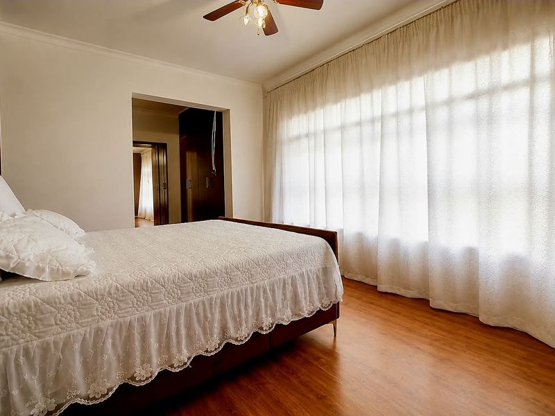 A well-maintained bedroom featuring laminate flooring, a ceiling fan, and built-in cupboards, with large windows allowing for ample natural light.