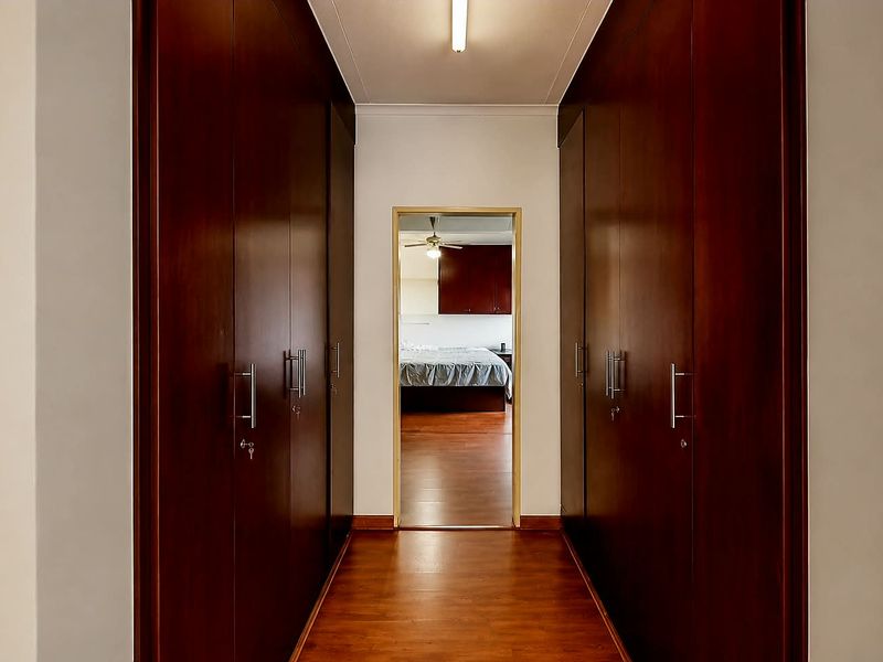A clean hallway featuring extensive floor-to-ceiling built-in wooden cupboards and laminate flooring, leading directly into an adjacent bedroom.