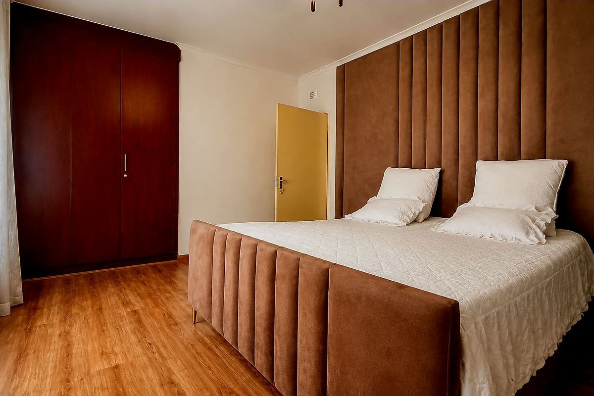 A well-maintained bedroom featuring laminate flooring, a large built-in wardrobe, and a decorative upholstered headboard wall panel.