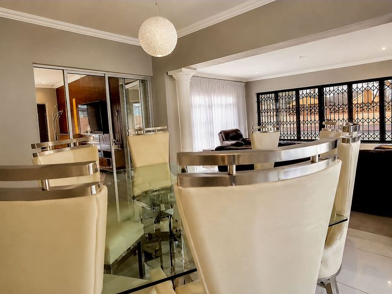 Spacious open-plan living and dining area featuring tiled floors, decorative columns, and large sliding doors with security gates for natural light.