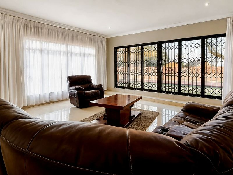 Spacious living room featuring polished tiled flooring, recessed lighting, and large sliding glass doors with security gates leading to the exterior.