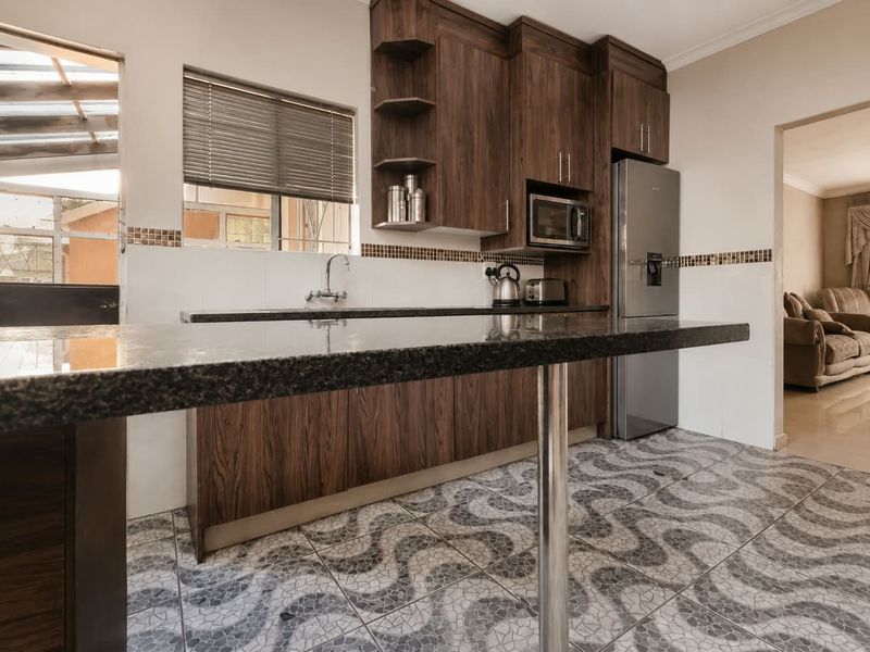 A functional kitchen featuring dark wood cabinetry, granite countertops, a tiled backsplash, and patterned floor tiles, with an open flow to the adjacent living area.