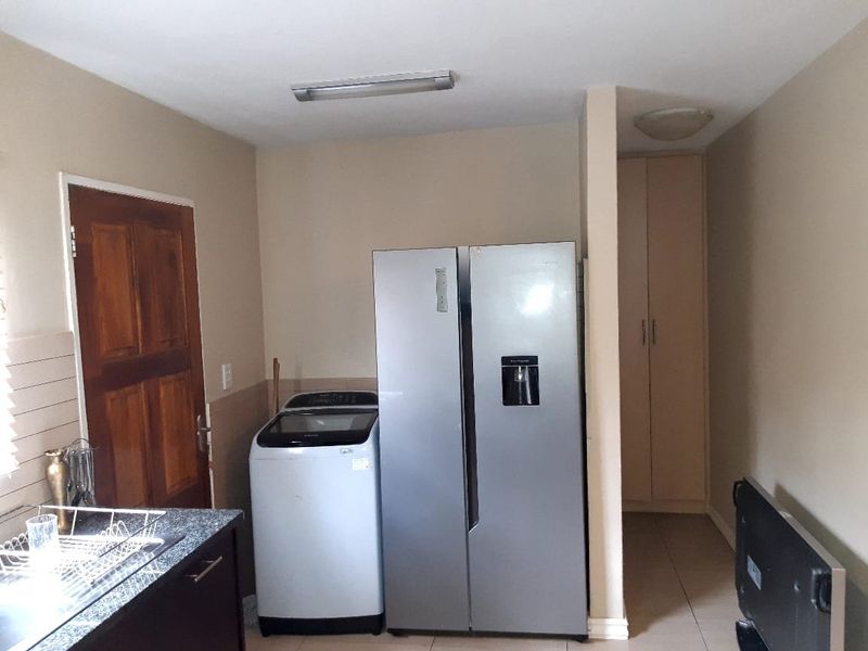 A functional kitchen area featuring built-in cabinetry, a countertop with a sink, and dedicated space for laundry and refrigeration appliances.