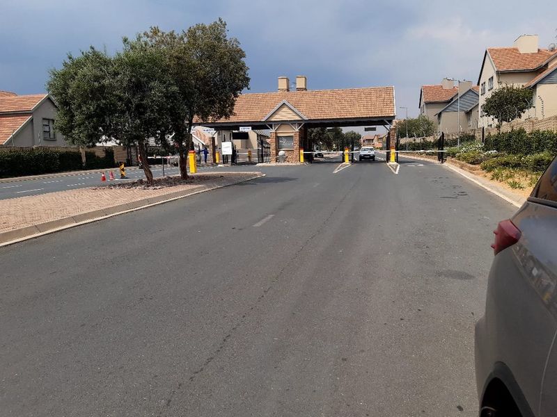 View of the secure residential estate entrance featuring a gated access point, boom barriers, and a brick-built security guardhouse.
