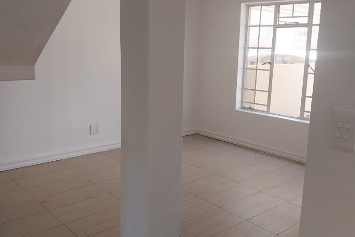 An empty, open-plan living area featuring neutral tiled flooring, a structural pillar, and natural light through a grid-pattern window.