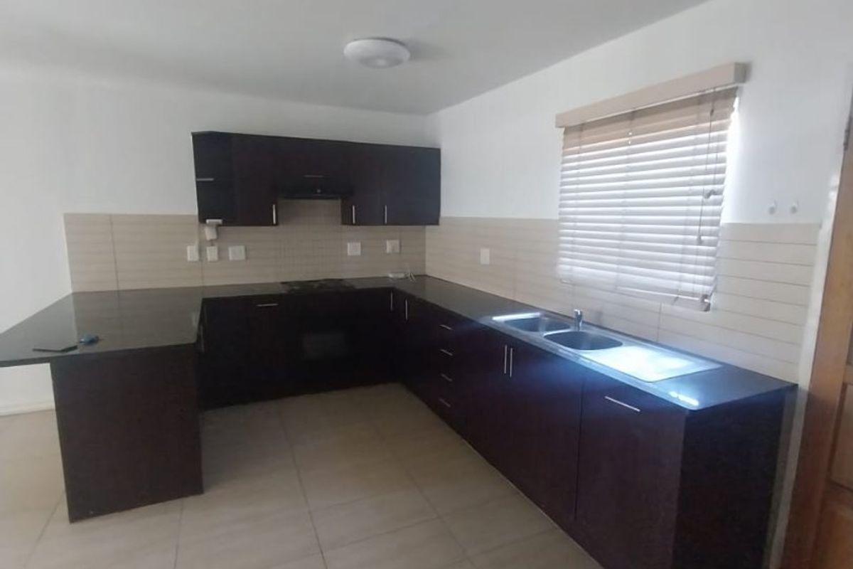 A clean, empty kitchen featuring dark wood cabinetry, granite countertops, built-in oven, hob, and a double sink with tiled backsplash.