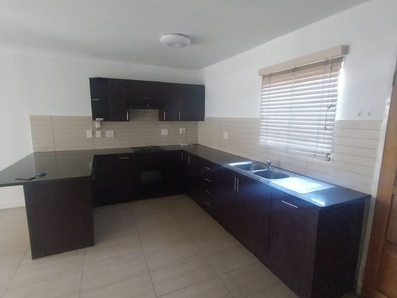 A clean, empty kitchen featuring dark wood cabinetry, granite countertops, built-in oven, hob, and a double sink with tiled backsplash.