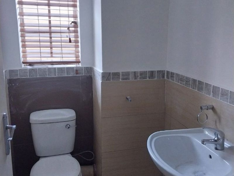 A compact bathroom featuring a pedestal basin and toilet, with partially tiled walls and a window fitted with wooden blinds.