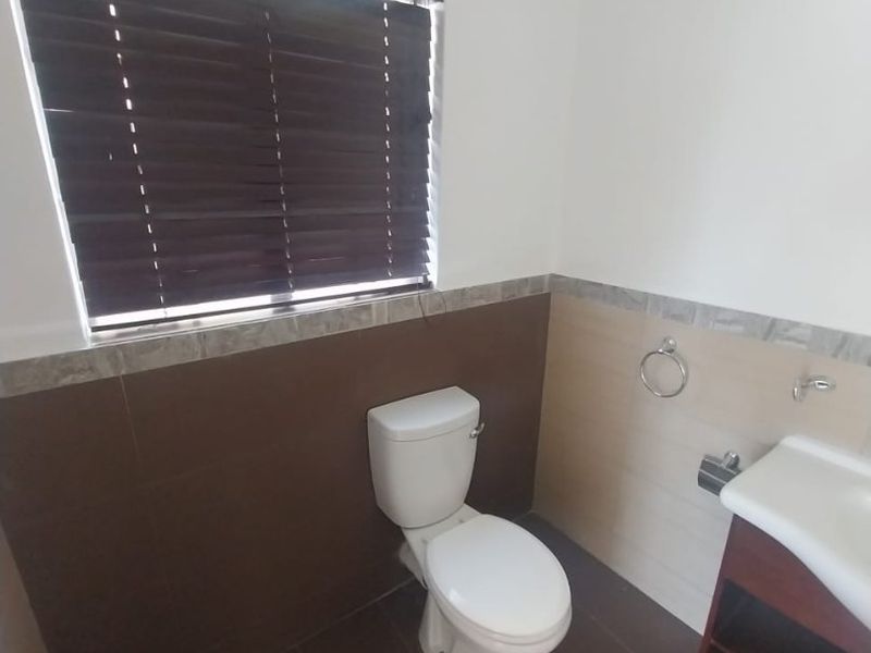 A compact bathroom featuring a toilet, vanity with basin, and tiled finishes, providing a functional space with neutral tones.