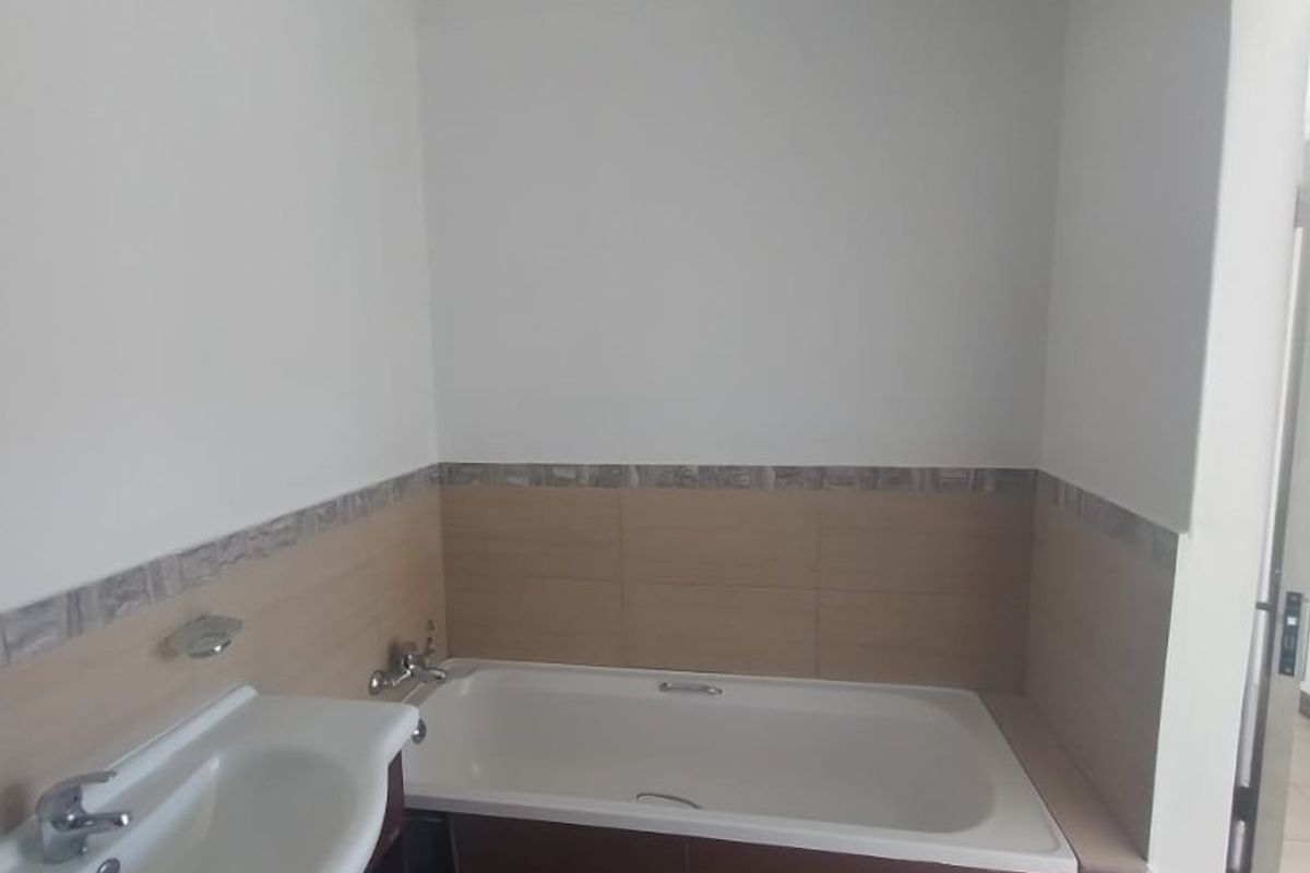 A functional bathroom featuring a built-in bathtub, vanity basin, and neutral wall and floor tiling.