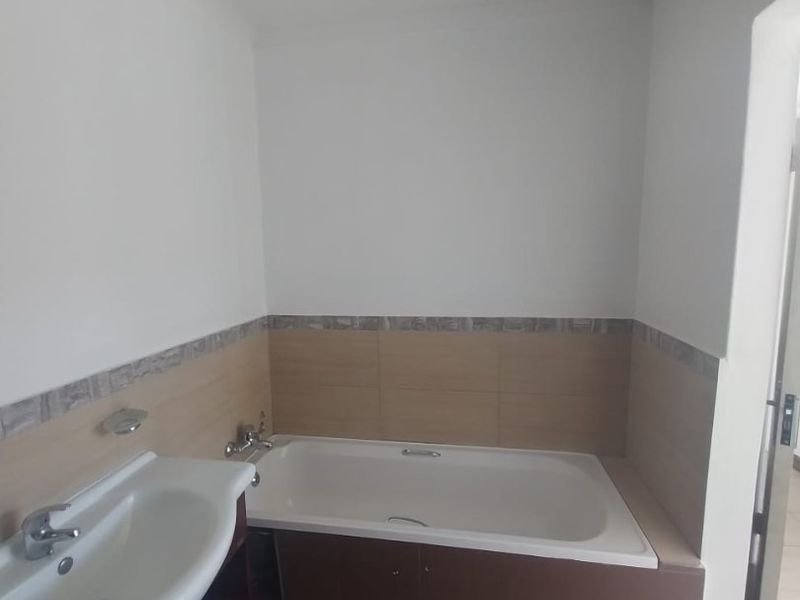 A functional bathroom featuring a built-in bathtub, vanity basin, and neutral wall and floor tiling.