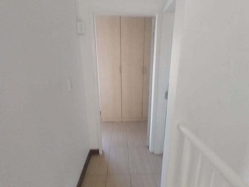 A bright, empty hallway featuring tiled flooring and built-in storage cupboards, leading towards a bedroom area.