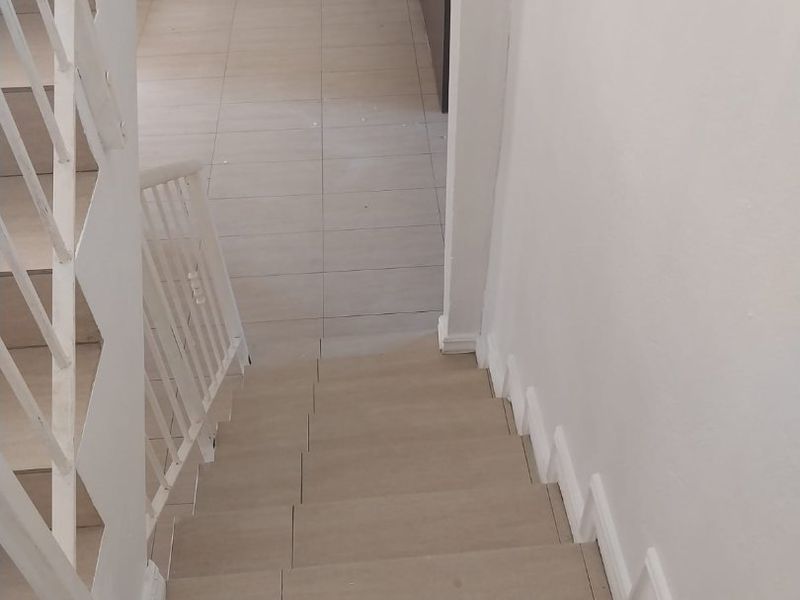 A view looking down a tiled staircase with a white metal balustrade, leading into an adjacent tiled living or kitchen area.
