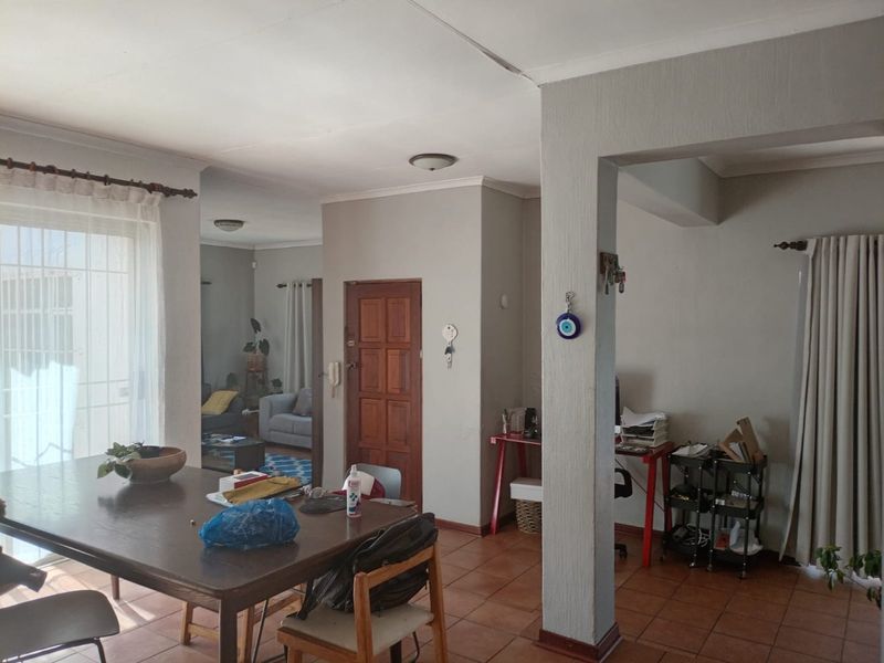 Open plan living and dining area featuring terracotta floor tiles, a wooden panel door, and access to an outdoor space via sliding glass doors.
