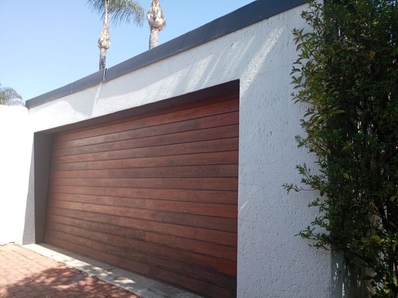 A view of a residential garage featuring a modern timber-slatted door and textured white exterior walls.