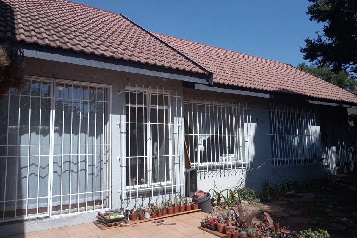 Rear view of the house featuring a tiled patio, sliding doors with security bars, and a pitched tiled roof.