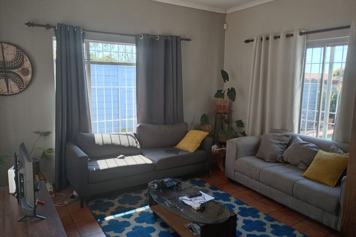 A comfortable living room featuring tiled flooring, large windows with security bars, and ample natural light.