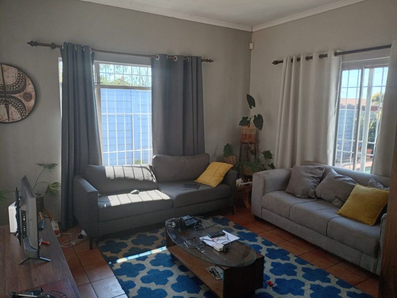 A comfortable living room featuring tiled flooring, large windows with security bars, and ample natural light.