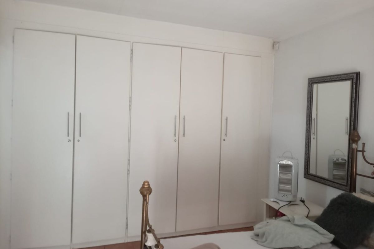 A bedroom featuring a wall of white built-in cupboards providing ample storage space.