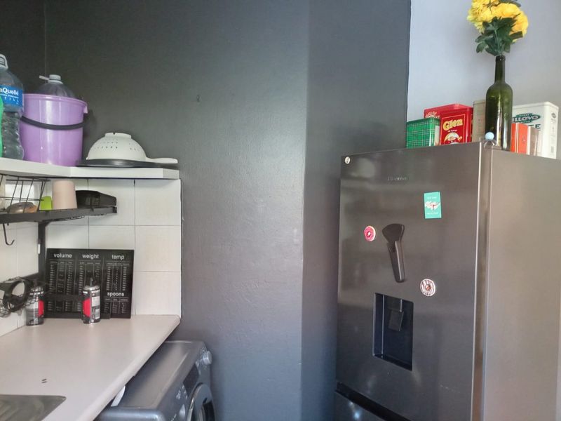 A functional kitchen corner featuring a tiled splashback, laminate countertop, and built-in shelving, providing practical utility space.