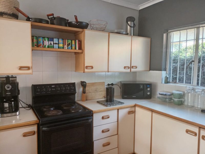 A functional kitchen featuring white cabinetry, laminate countertops, a tiled backsplash, and an electric stove with a window providing natural light.