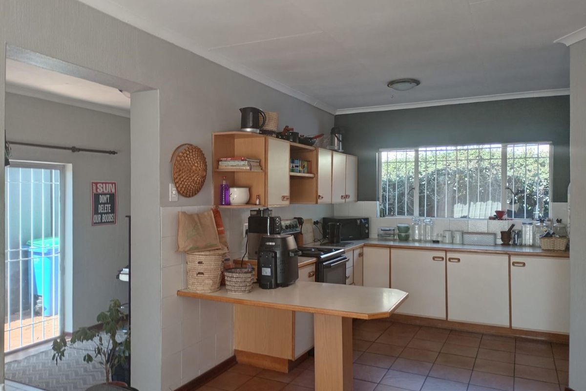 A functional kitchen featuring tiled flooring, built-in cabinetry with a breakfast counter, and a window with security bars, offering a practical layout.