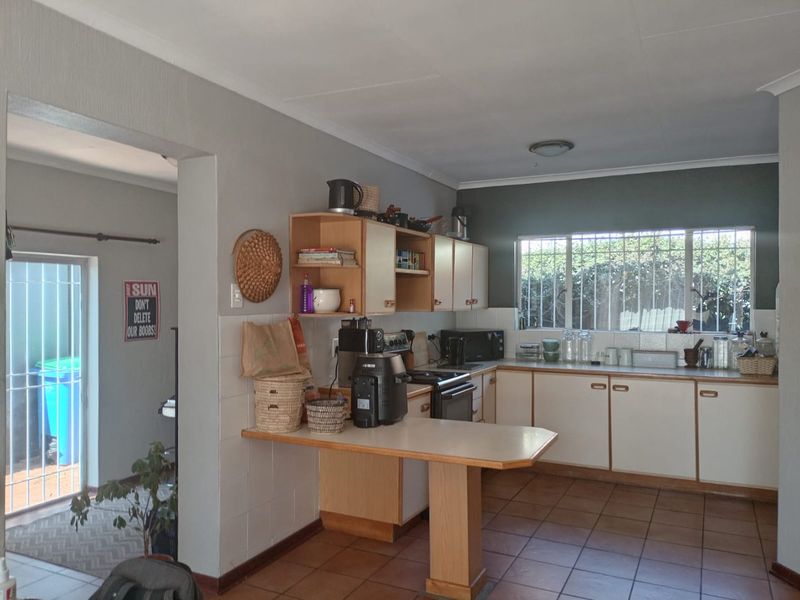 A functional kitchen featuring tiled flooring, built-in cabinetry with a breakfast counter, and a window with security bars, offering a practical layout.