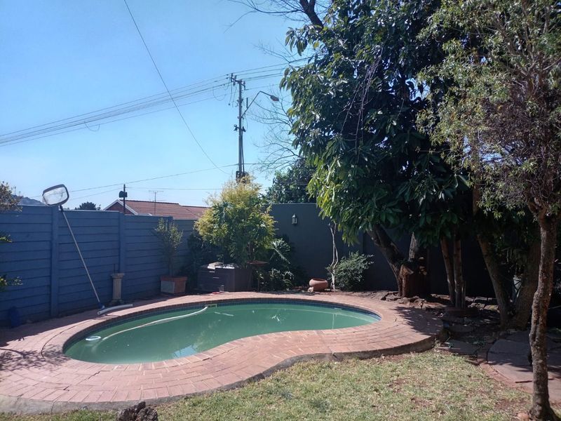 A private backyard featuring a kidney-shaped swimming pool with brick coping, surrounded by established trees and perimeter fencing.