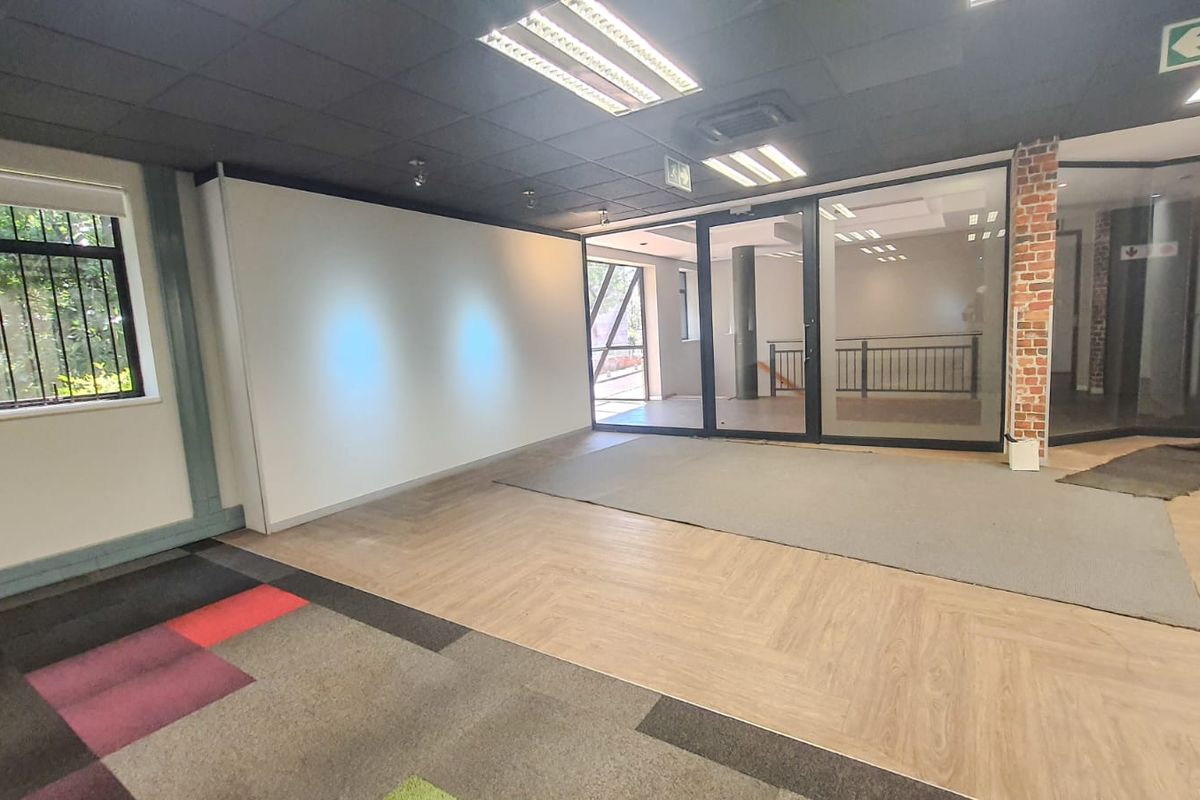 Open-plan commercial office space featuring a mix of laminate and carpet flooring, glass partitions, and an exposed brick accent column.