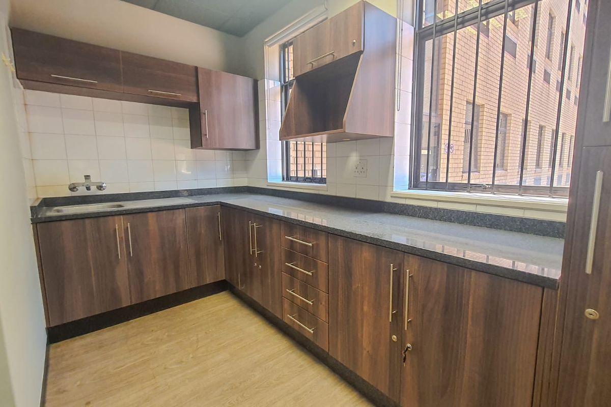 A clean, functional kitchen area featuring dark wood-look cabinetry, granite countertops, a stainless steel sink, and secure window bars.