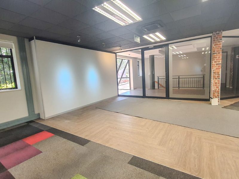 Open-plan commercial office space featuring a mix of laminate and carpet flooring, glass partitions, and an exposed brick accent column.