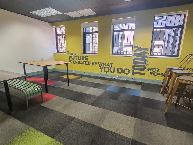 A commercial office space featuring carpet tiles, security bars on windows, and a drop ceiling, suitable for a collaborative work environment.